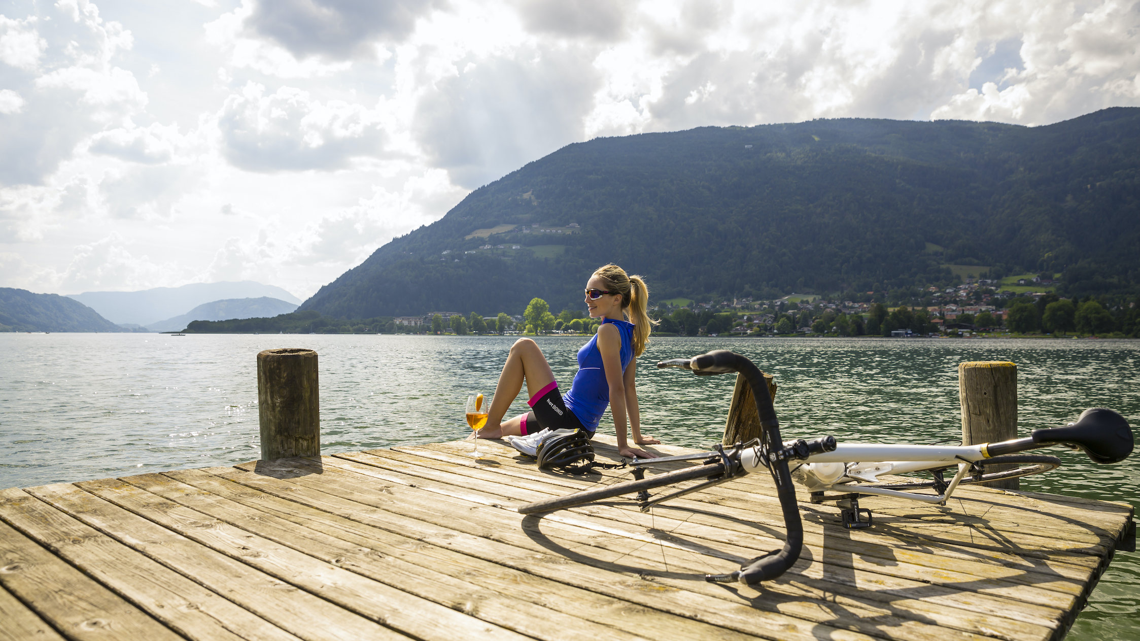 Radfahrerin sitz am Steg und blickt auf den Ossiacher See