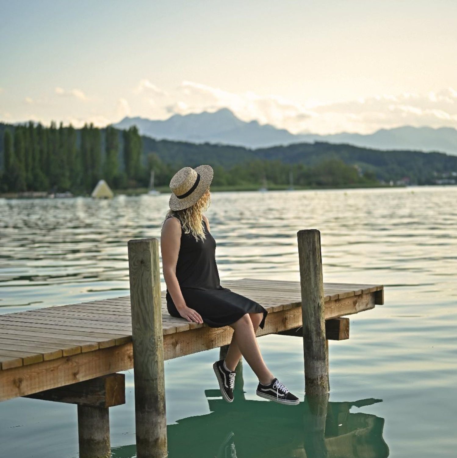 Frau sitzt am Steg eines Sees