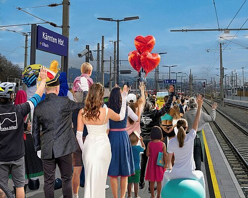 Gruppe von Menschen steht am Villacher Hauptbahnhof, im Hintergrund sieht man das Bahnhofsschild mit der Aufschrift "Kärnten HBF"