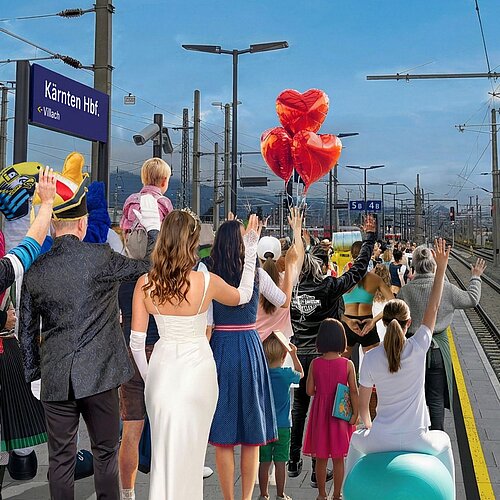 Gruppe von Menschen steht am Villacher Hauptbahnhof, im Hintergrund sieht man das Bahnhofsschild mit der Aufschrift "Kärnten HBF"