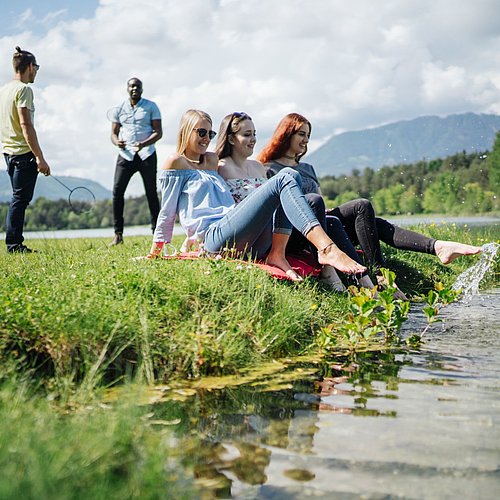 Studierende sitzen in der Wiese am Fluss
