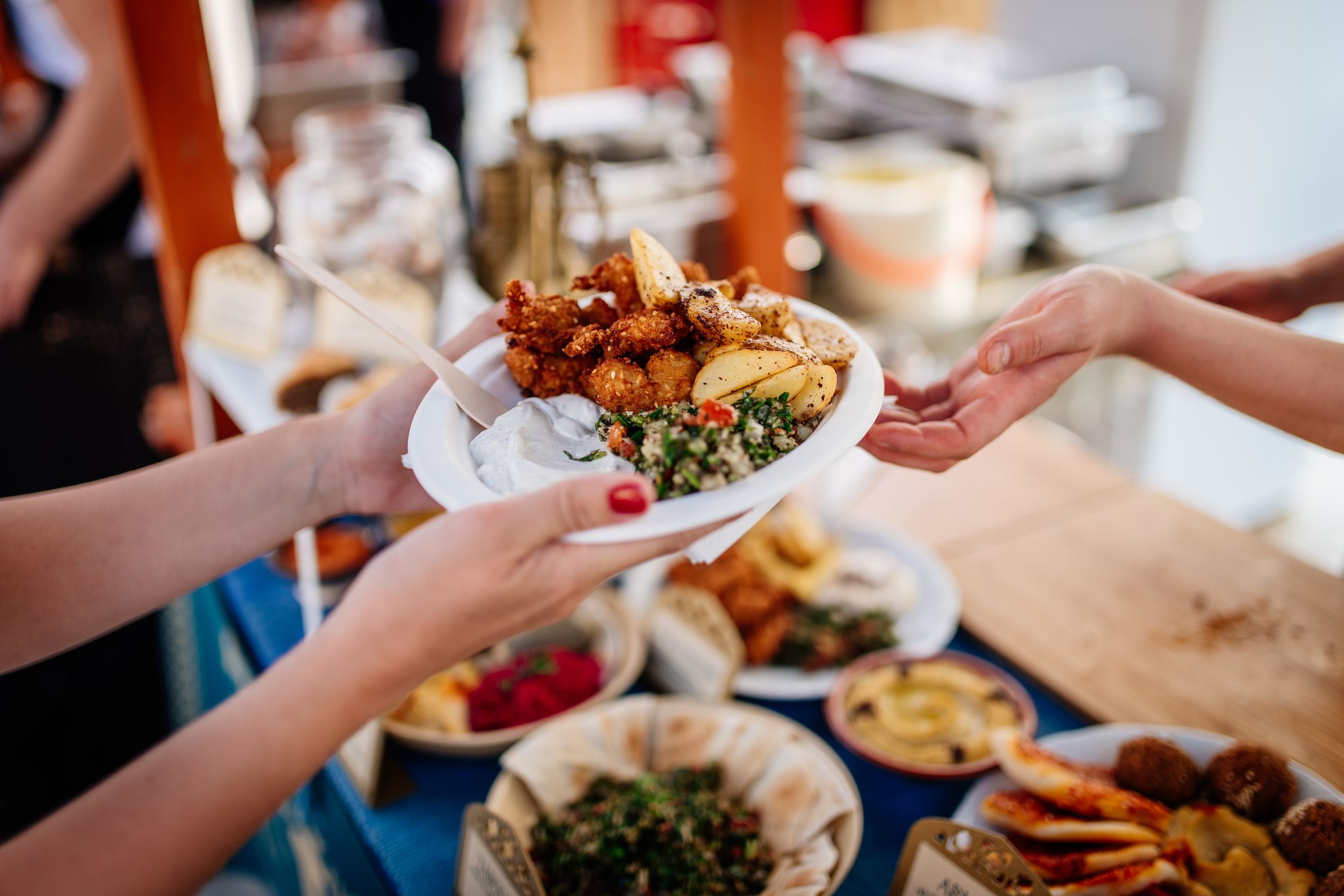 A woman gives another woman a plate full of food from the market stall