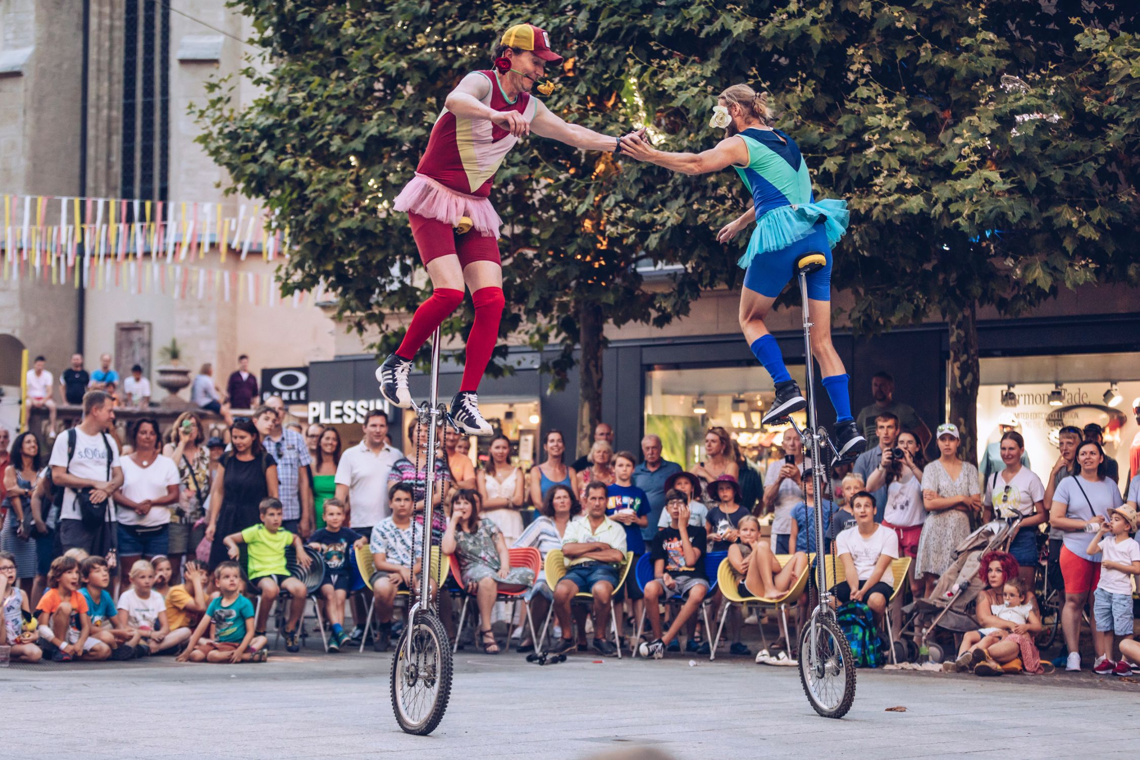 Two artists on unicycles surrounded by enthusiastic spectators